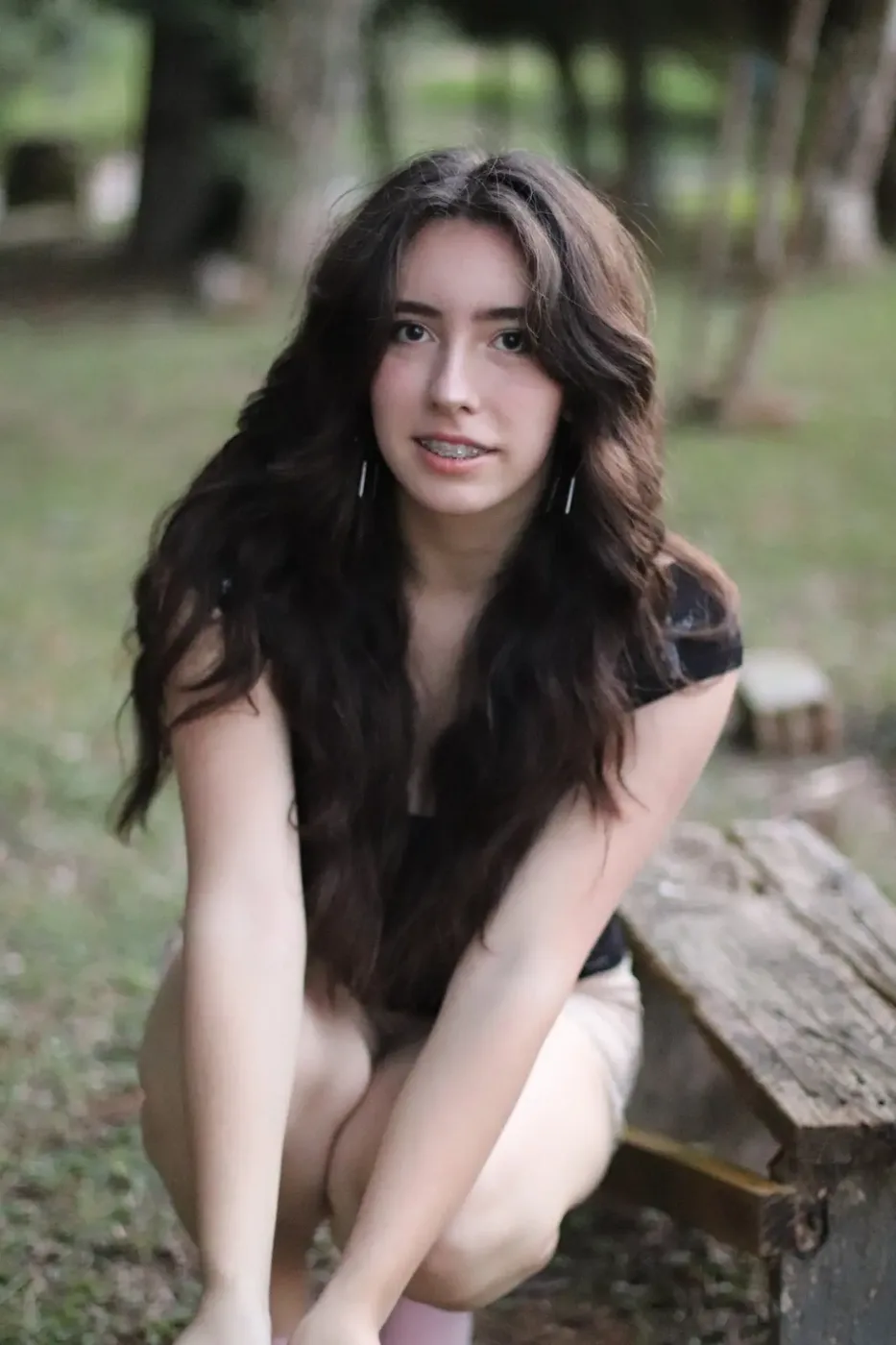 Garota de cabelos longos sorrindo em um bosque durante ensaio fotográfico