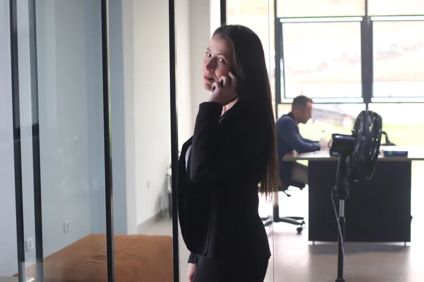 Profissional ao telefone em escritório com colega trabalhando ao fundo