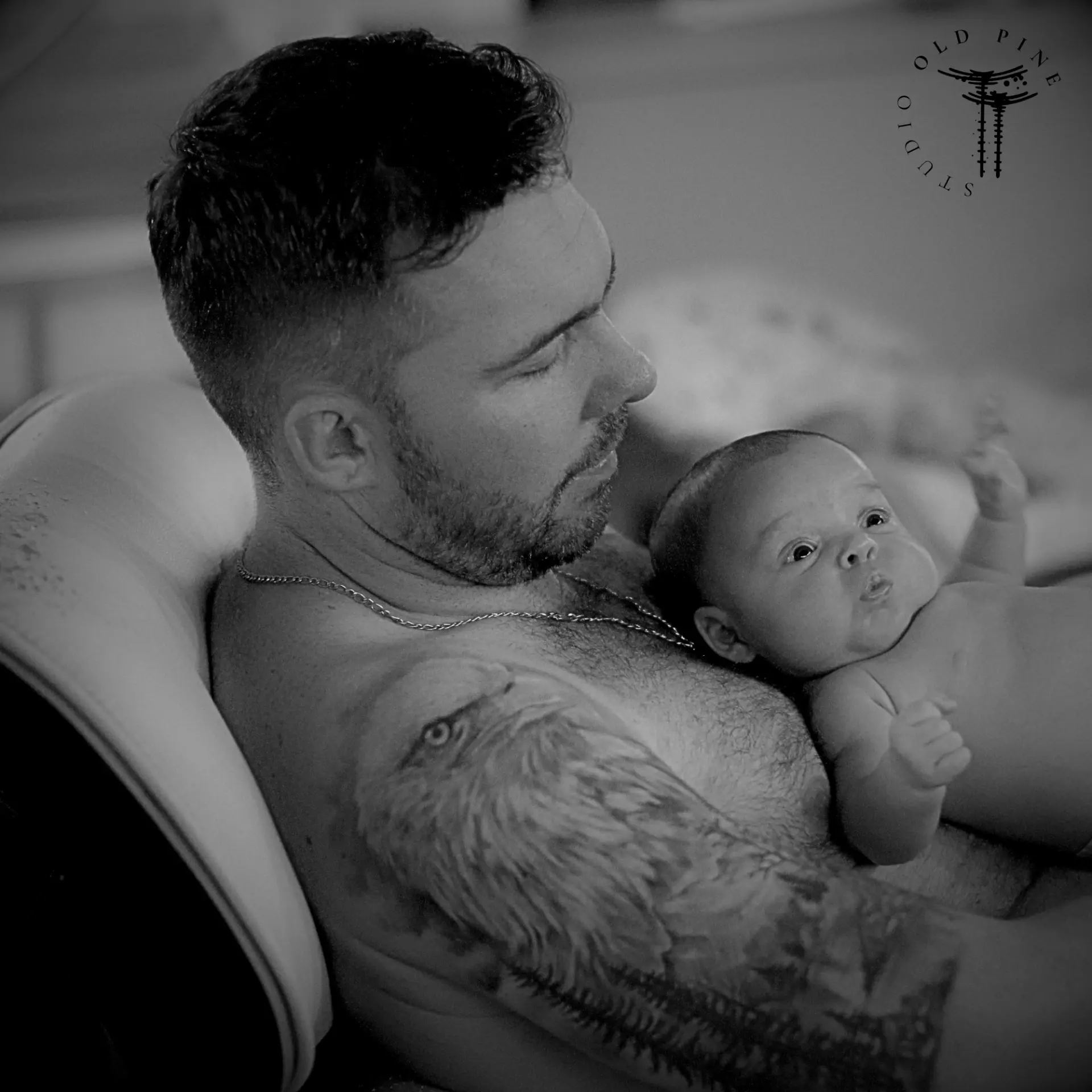 Pai tatuado com o bebê no colo em fotografia preto e branco